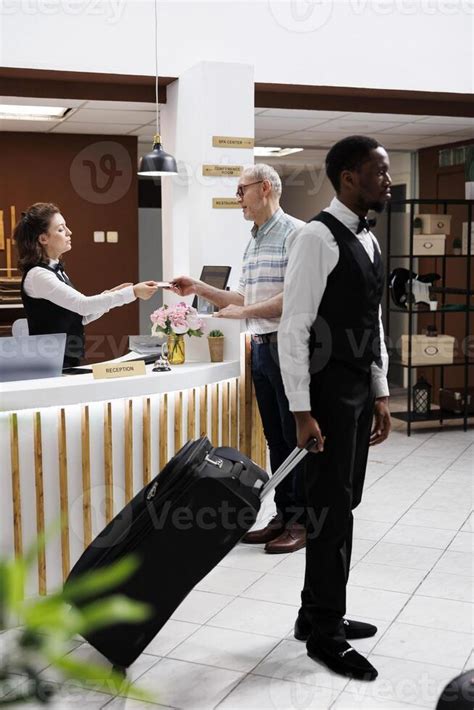 Female Concierge Assists Elderly Man At Front Desk Providing Smooth Checkin Process And Female Concierge Assists Elderly Man At Front Desk Providing Smooth Checkin Process And